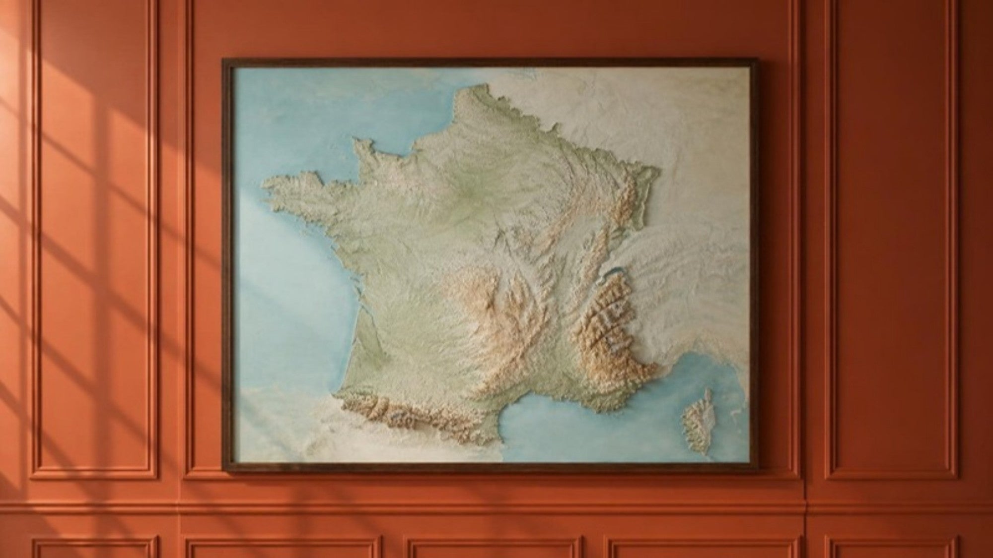 Framed relief map of France hanging on a terracotta wall
